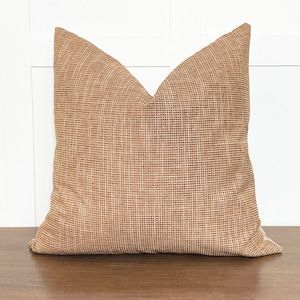 May include: A brown woven throw pillow with a subtle texture. The pillow is square and has a simple design.