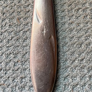 May include: A silver dinner knife with a star design on the handle. The knife is made of stainless steel and has a slightly curved blade.