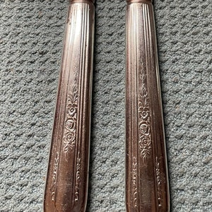 May include: Two silver dinner knives with floral designs on the handles. The knives are made of stainless steel and have a polished finish.