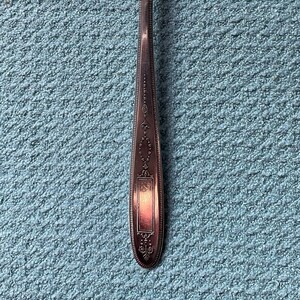 May include: A silver fork with an ornate design on the handle. The fork has three tines and a rounded handle with a decorative pattern.