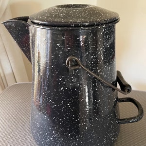 May include: Black enamel camping coffee pot with white speckles. The pot has a lid, a handle, and a spout.