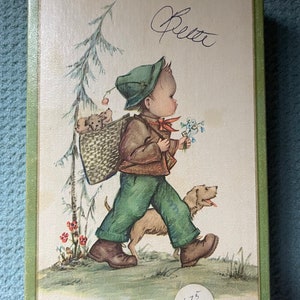 May include: A vintage illustration of a boy wearing a green hat and brown jacket walking with a dog. He is carrying a basket with three puppies inside. The illustration is on a cream-colored background with a green border. The number 175 is written on a white circle in the bottom right corner.