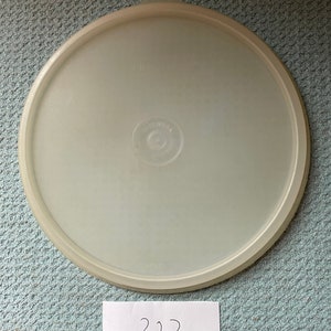 May include: A white plastic lid with a small round knob on top. The lid has a smooth surface and a slightly raised edge. The number "227" is written on a piece of paper below the lid.