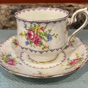 May include: A white teacup and saucer set with a floral pattern. The cup and saucer have a gold trim and a delicate floral design with pink, yellow, and blue flowers.