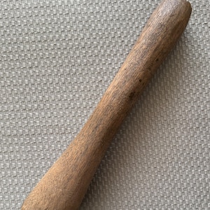 May include: A wooden pestle, cylindrical in shape, with a rounded handle and a slightly wider base. The pestle is a medium brown color and has visible wood grain. It is designed for grinding ingredients in a mortar.