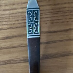 May include: A silver and brown handled butter knife with a decorative design of repeating swirls.