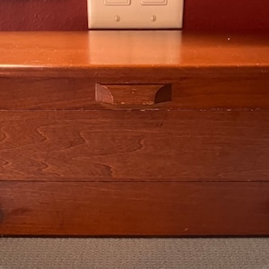 May include: A wooden box with two drawers and brass handles. The box is made of a light brown wood with a grain pattern.