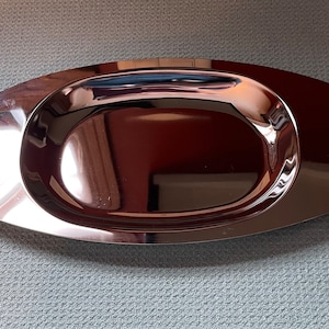 May include: A silver oval serving tray with two gold handles. The tray has a raised rim and a smooth, reflective surface.