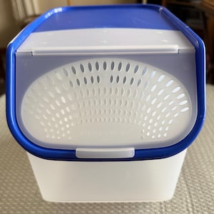 May include: A blue and white plastic container with a vented lid. The lid has a white plastic handle and the container has the word "Rubbermaid" printed on the front.