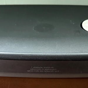 May include: A rectangular food storage container with a black lid and a clear base. The lid has a white, circular button and the brand name is visible. The container is designed for food storage and organization.