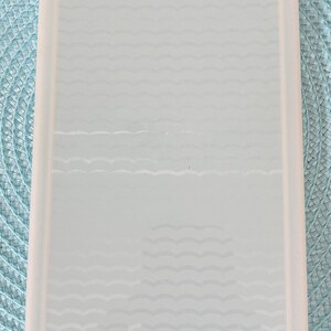 May include: A rectangular, light blue Tupperware container with a wavy pattern on the interior. The container has a white rim and is set against a light blue patterned background.