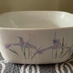 May include: White ceramic baking dish with a square shape and two handles. The dish has a floral design featuring purple and green irises.