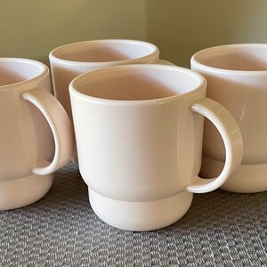 May include: Set of four off-white ceramic mugs with a stacked design. Each mug has a rounded handle.