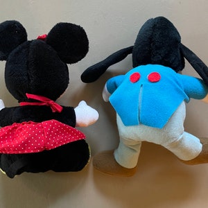 May include: Two plush toys, one black with a red polka dot skirt and the other black with blue and white clothing. Both toys have large black ears.