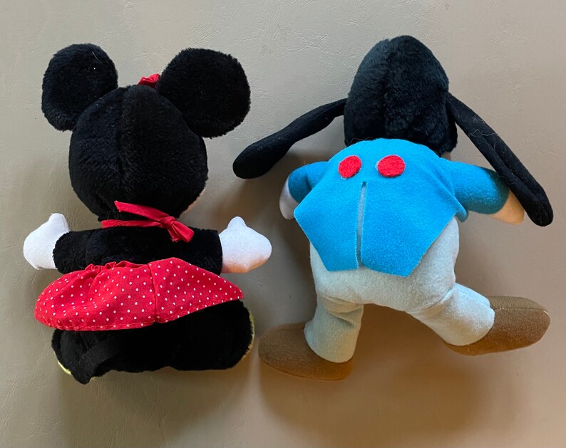 May include: Two plush toys, one black with a red polka dot skirt and the other black with blue and white clothing. Both toys have large black ears.