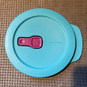 May include: A light blue plastic container lid with a purple measuring spoon attached to the lid. The lid has the word "Tupperware" printed on it.