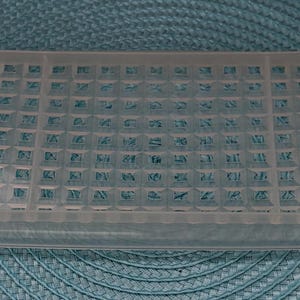 May include: A clear, rectangular plastic tray with a grid pattern. The tray has slightly raised edges and handles on each end. The grid is composed of small, square indentations. The tray is designed for kitchen use.