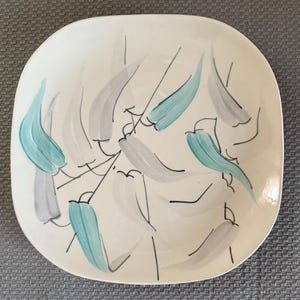 May include: Square ceramic serving dish with a white background. The dish is decorated with stylized gray and teal leaf-like shapes and black lines. The dish has rounded corners.