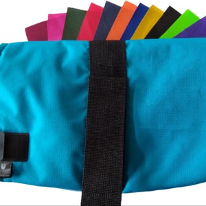 May include: A turquoise dog coat with black adjustable straps. The coat is made of a water-resistant material and has a velcro closure.