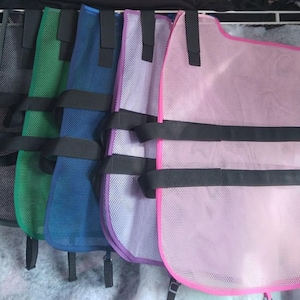 May include: A row of mesh vests in various colors: gray, green, blue, purple, and pink. Each vest has black straps and trim. The vests are hanging, showcasing their design and color variations.