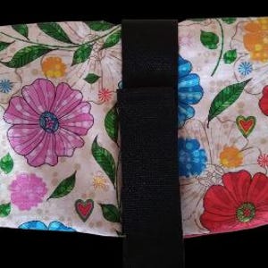 May include: A floral patterned wrap with a black strap and closure. The wrap features a cream background with large pink, red, and blue flowers, green leaves, and small hearts. The wrap is designed to fit around an object.