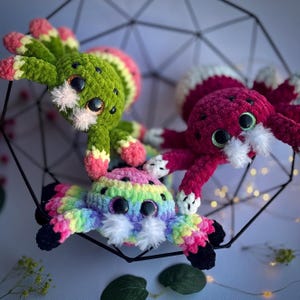 Puede incluir: Tres juguetes de araña de crochet en una variedad de colores, incluyendo verde, rosa y rojo. Las arañas tienen ojos grandes y saltones y hilo blanco para sus bocas.