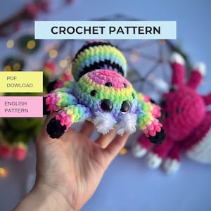 May include: A crochet pattern PDF download for a plush spider toy. The spider features a rainbow-colored body with black stripes, large black eyes, and white fuzzy accents. Text on the image reads CROCHET PATTERN, PDF DOWLOAD, and ENGLISH PATTERN.