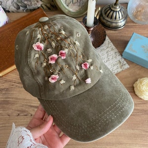 May include: A green baseball cap with pink embroidered flowers and vines. The cap has a curved brim and a traditional baseball cap shape.