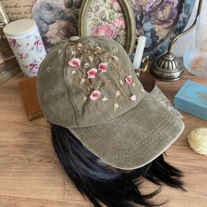 May include: A green baseball cap with pink embroidered flowers and vines. The cap has a curved brim and a mesh back.