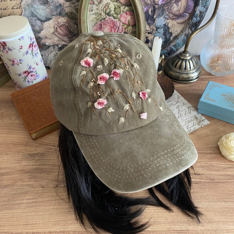 May include: A green baseball cap with embroidered pink flowers and vines. The cap has a curved brim and a mesh back.
