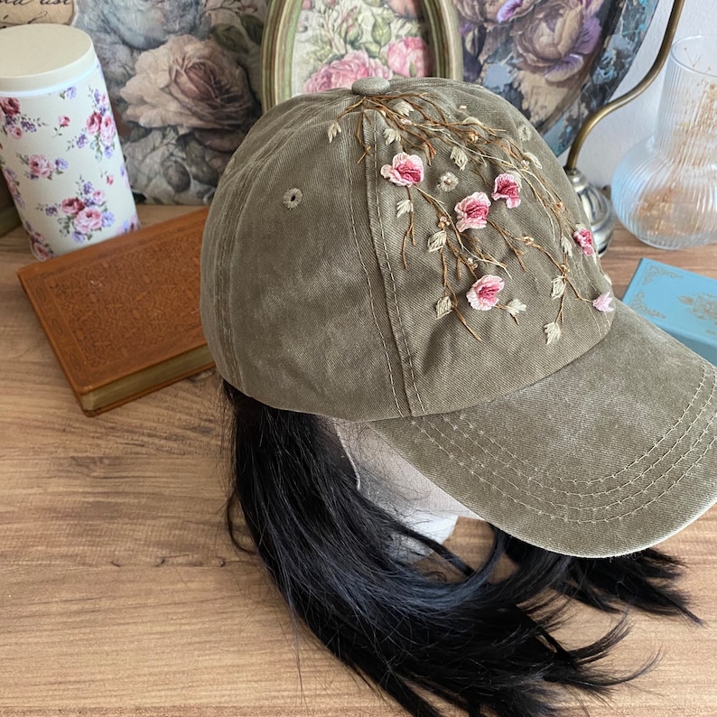 May include: A green baseball cap with embroidered pink flowers and vines. The cap has a curved brim and a mesh back.