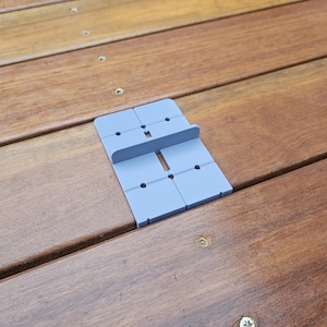 May include: A light blue plastic spacer with a raised section in the middle. The spacer is designed to be used on a wooden deck to create a gap between the deck boards.