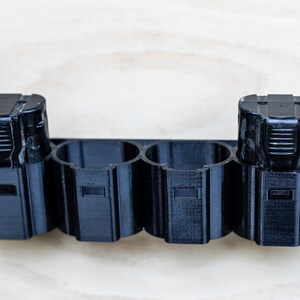 K&ouml;nnte beinhalten: Ein schwarzer Batteriehalter aus Kunststoff mit vier Steckpl&auml;tzen zum Aufbewahren von Batterien. Zwei Batterien befinden sich im Halter.
