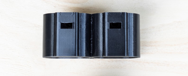 K&ouml;nnte beinhalten: Zwei schwarze Kunststoffstecker mit rechteckigen &Ouml;ffnungen.