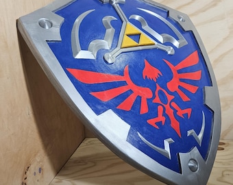 May include: A blue, silver, and red shield with a stylized design. The shield features a central emblem with a yellow triangle and a red bird-like figure. The shield has a silver border and rivets.