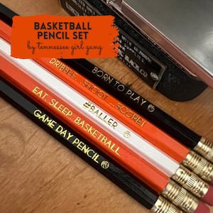 May include: Set of five black and orange pencils with gold lettering. The pencils have basketball-themed sayings, including "Born to Play", "Dribble...Shoot...Scope!" and "Game Day Pencil".