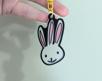 May include: A white bunny keychain with black outlines and pink ears. The keychain is attached to a yellow chain.