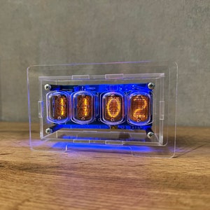 Könnte beinhalten: Ein transparentes Acrylgehäuse mit blauem Licht beleuchtet vier Nixie-Röhren, die die Zahl 1102 anzeigen.