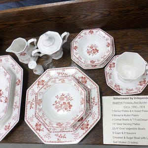 May include: A set of red and white floral patterned china dinnerware, including plates, bowls, and a creamer and sugar bowl. The set is labeled "Bittersweet by Independence" and includes the text "Red Pink Flowers, Red Border Design, Circa 1950-1974".
