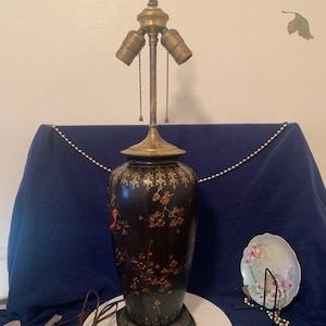 May include: A black and gold table lamp with a floral design and a three-way socket. The lamp is on a white surface.