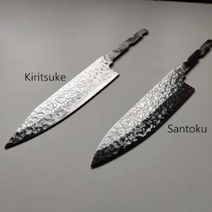 Può includere: Due coltelli da cucina giapponesi, un Kiritsuke e un Santoku, sono esposti su una superficie grigia. Le lame hanno una texture martellata. Il coltello Kiritsuke è a sinistra e il coltello Santoku è a destra. I nomi dei coltelli sono scritti sull'immagine.