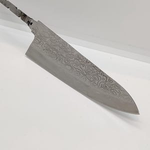 Könnte beinhalten: Ein Edelstahl-Kochmesser mit gemusterter Klinge und strukturiertem Griff. Die Klinge hat ein einzigartiges Wirbeldesign. Das Messer ist für den professionellen oder privaten Gebrauch konzipiert.