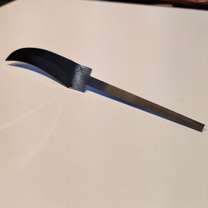 K&ouml;nnte beinhalten: Eine silberne Messerklinge mit einer gebogenen Kante und einem geraden Griff. Die Klinge tr&auml;gt eine kleine Inschrift mit der Aufschrift "NE".