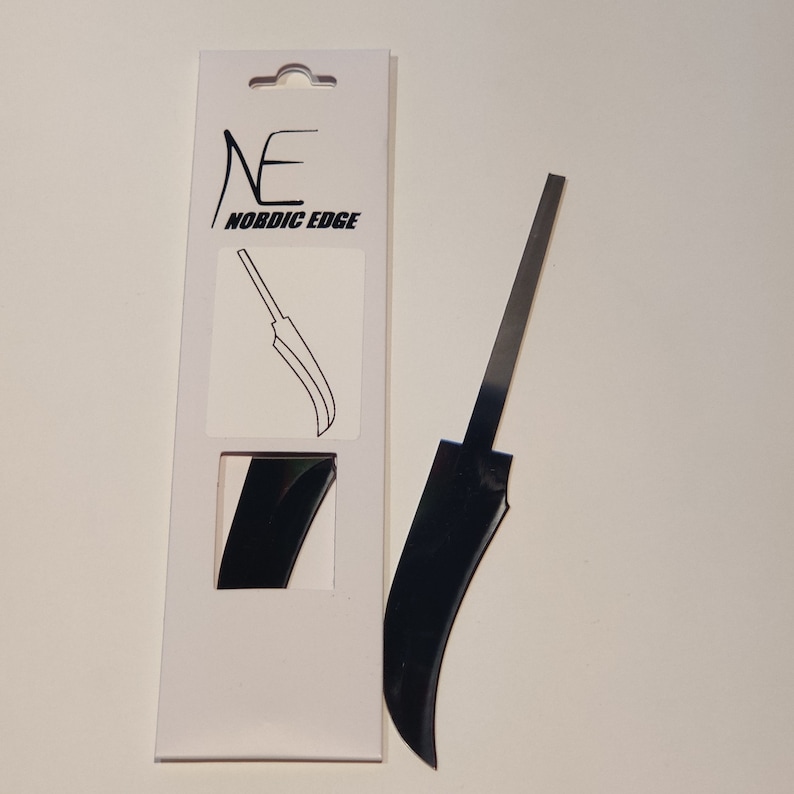 K&ouml;nnte beinhalten: Eine schwarze Messerklinge mit einer gebogenen Kante, verpackt in einer wei&szlig;en Schachtel mit dem Text "NE NORDIC EDGE".