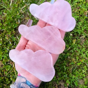 Könnte beinhalten: Drei rosa wolkenförmige Gua Sha-Werkzeuge aus Rosenquarz. Die Werkzeuge bestehen aus glattem, poliertem Rosenquarz und sind für die Gesichtsmassage konzipiert.