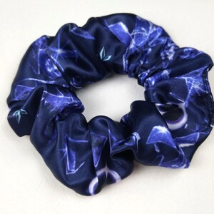 Puede incluir: Una goma para el pelo azul marino con un estampado de formas geométricas blancas y azules. La goma para el pelo está hecha de un material sedoso y está fruncida para crear un efecto de volantes. Es un accesorio para el cabello.