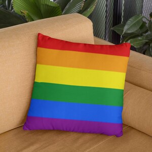 Könnte beinhalten: Ein Regenbogen-Wurfkissen mit sechs horizontalen Streifen. Das Kissen liegt auf einem hellbraunen Sofa.