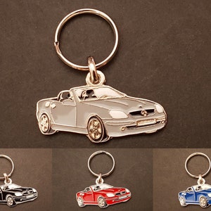 Puede incluir: Un llavero de metal plateado, rojo y azul con un modelo detallado de un coche deportivo convertible. El llavero tiene un anillo plateado para sujetarlo a las llaves.