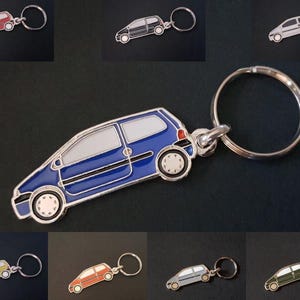 Puede incluir: Un llavero azul con forma de coche con borde plateado y un llavero plateado. El llavero tiene ventanas blancas y neumáticos negros. También se muestran llaveros adicionales en rojo, negro, gris, verde y amarillo.