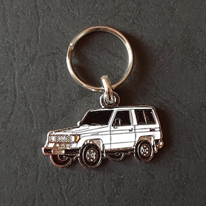 May include: A silver keychain featuring a white Toyota Land Cruiser. The keychain has a silver ring for attaching to keys.